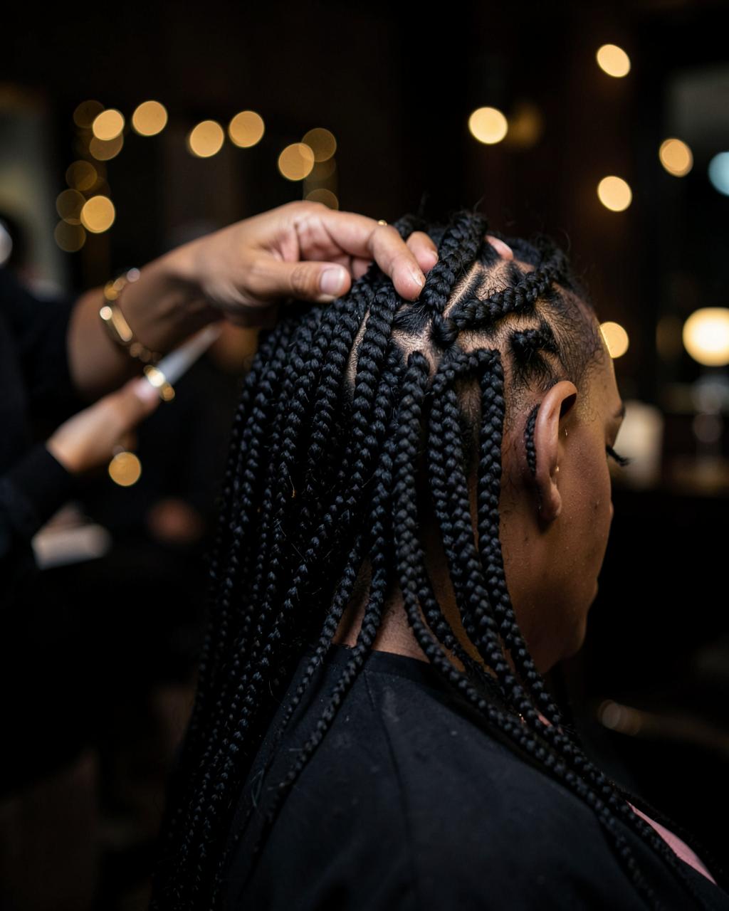 Braider's hands installing long knotless braids on a client