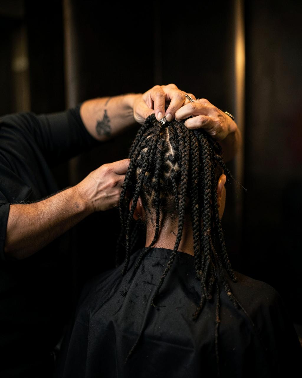 Loctician styling a client's locs in a dark studio