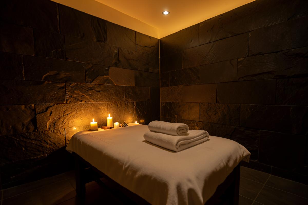 Candlelit spa treatment room with folded towels on a dressed massage table